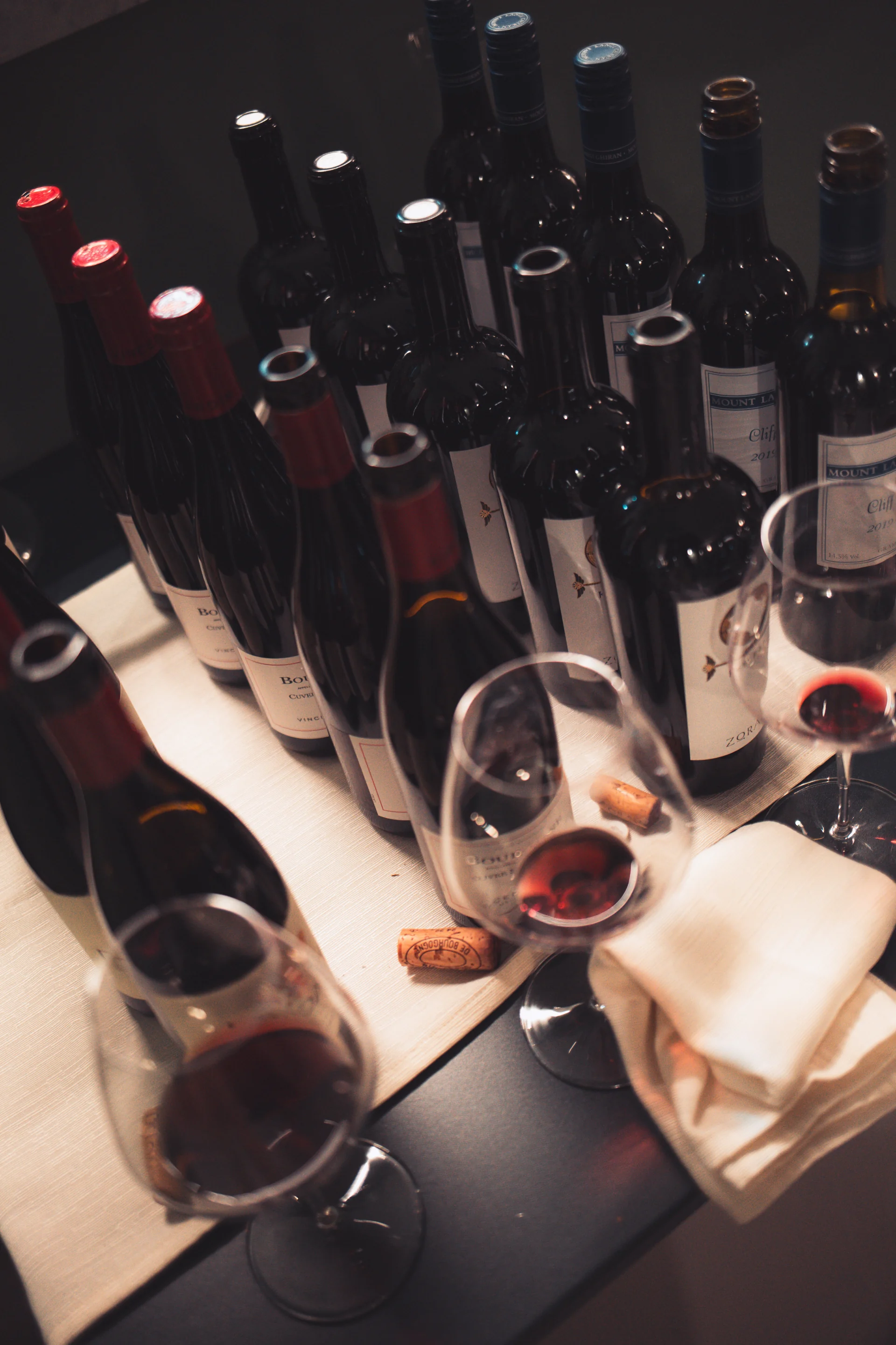 Fila di bottiglie di vino stappate con calici e tappi di sughero durante una degustazione multipla